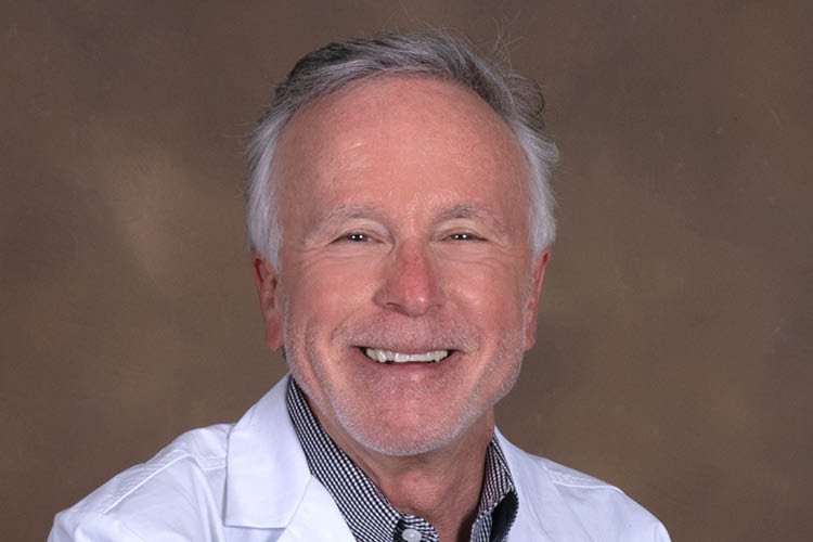 Dr. Jerman smiling in a white lab coat on a brown background