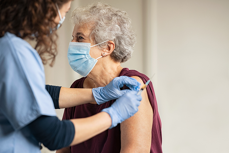 A nurse gives a shot to an older woman wearing a surgical mask