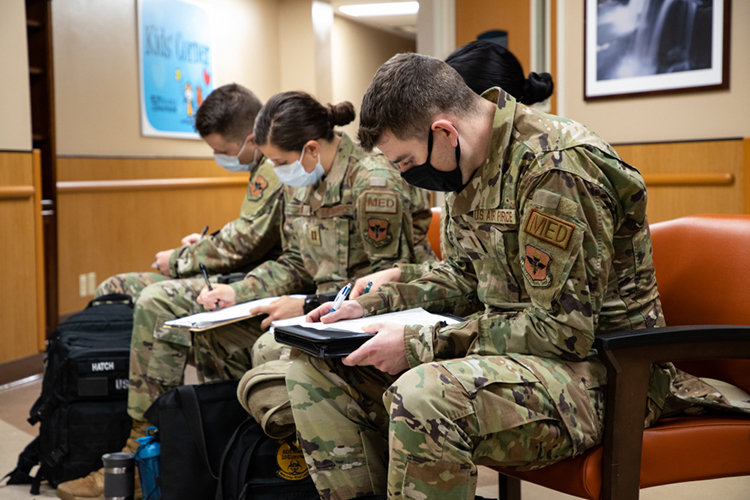 Uniformed air force personnel sit and fill out paperwork in a hospital lobby