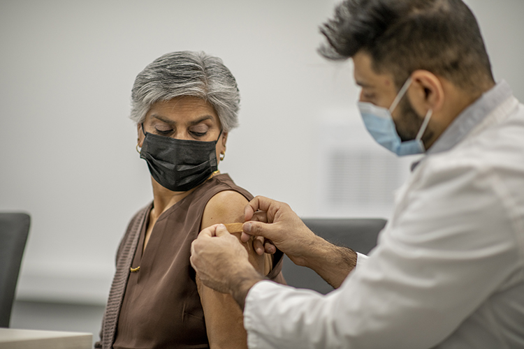 A masked healthcare provider bandages the arm of a masked woman