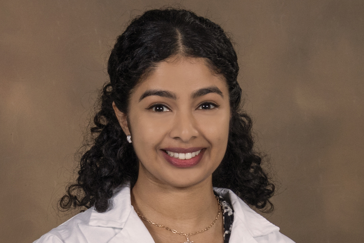 Dr. James smiles in a white coat before a tan background