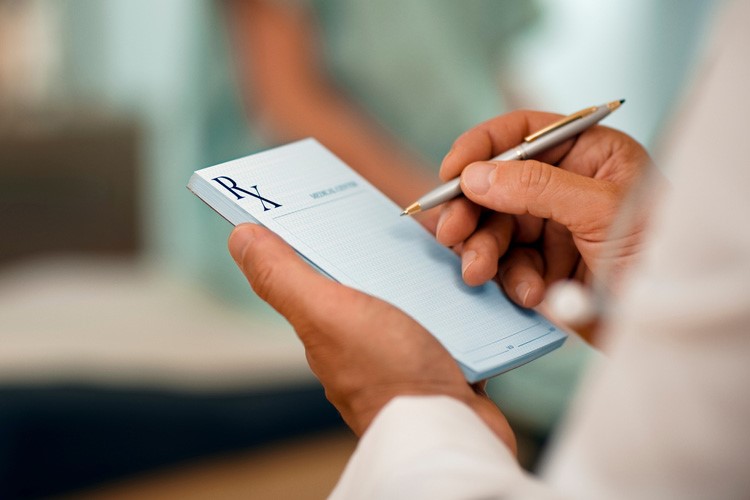 a close-up of a person's left hand holding a prescription pad and the right hand holding a pen