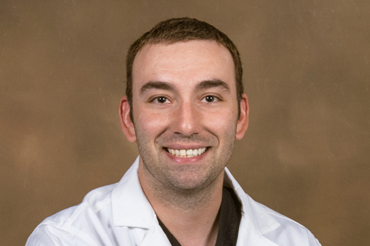 Dr. Vieira smiles in a white lab coat before a tan background