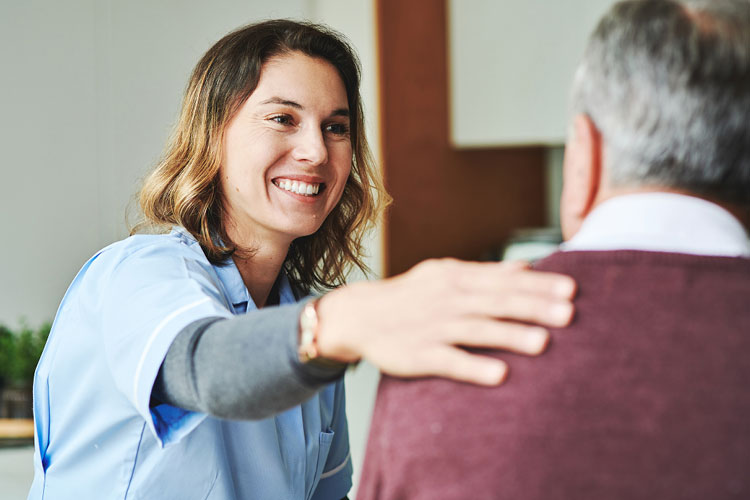 a smiling woman sitting across from a man places her hand his shoulder