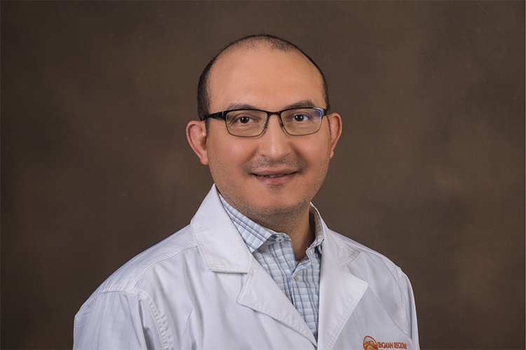 Dr. Mahgoub smiles in a white coat before a tan background