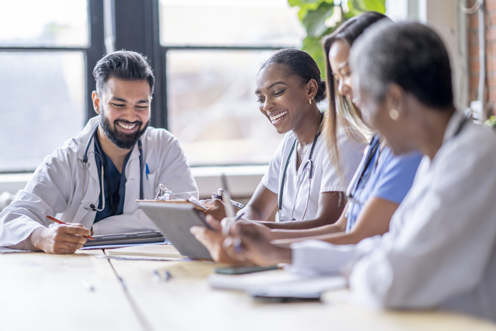 four medical professionals at a table reviewing clipboards and smiling