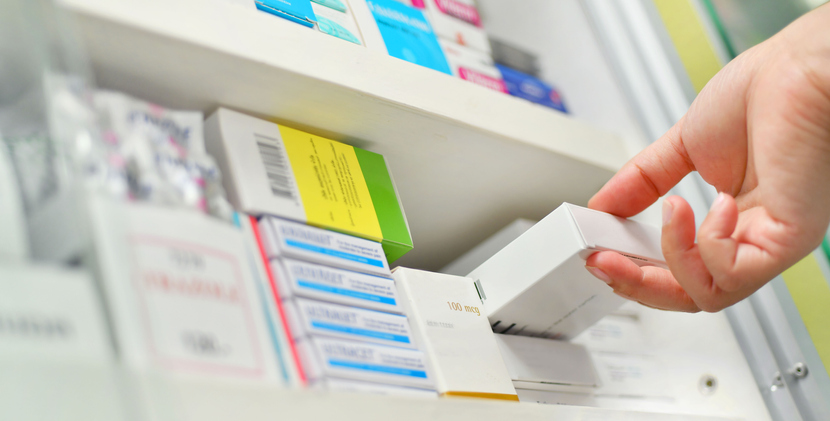 A hand pulls a box of medication from a stocked shelf