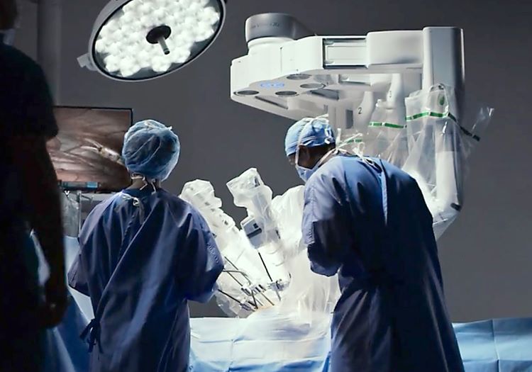 people dressed in surgical scrubs are shown from behind in a bright operating room