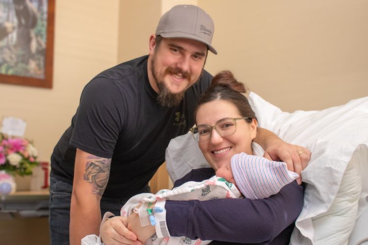 a dad and mom smiling at the camera holding their newborn baby