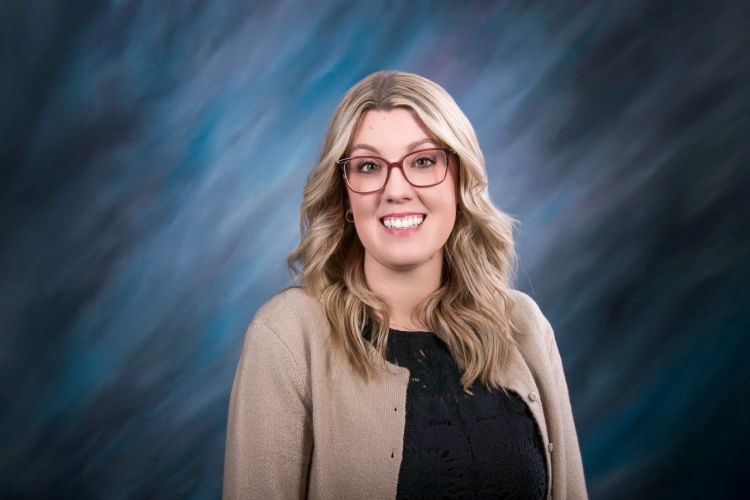 Erin Black, FNP, smiles before a blue background